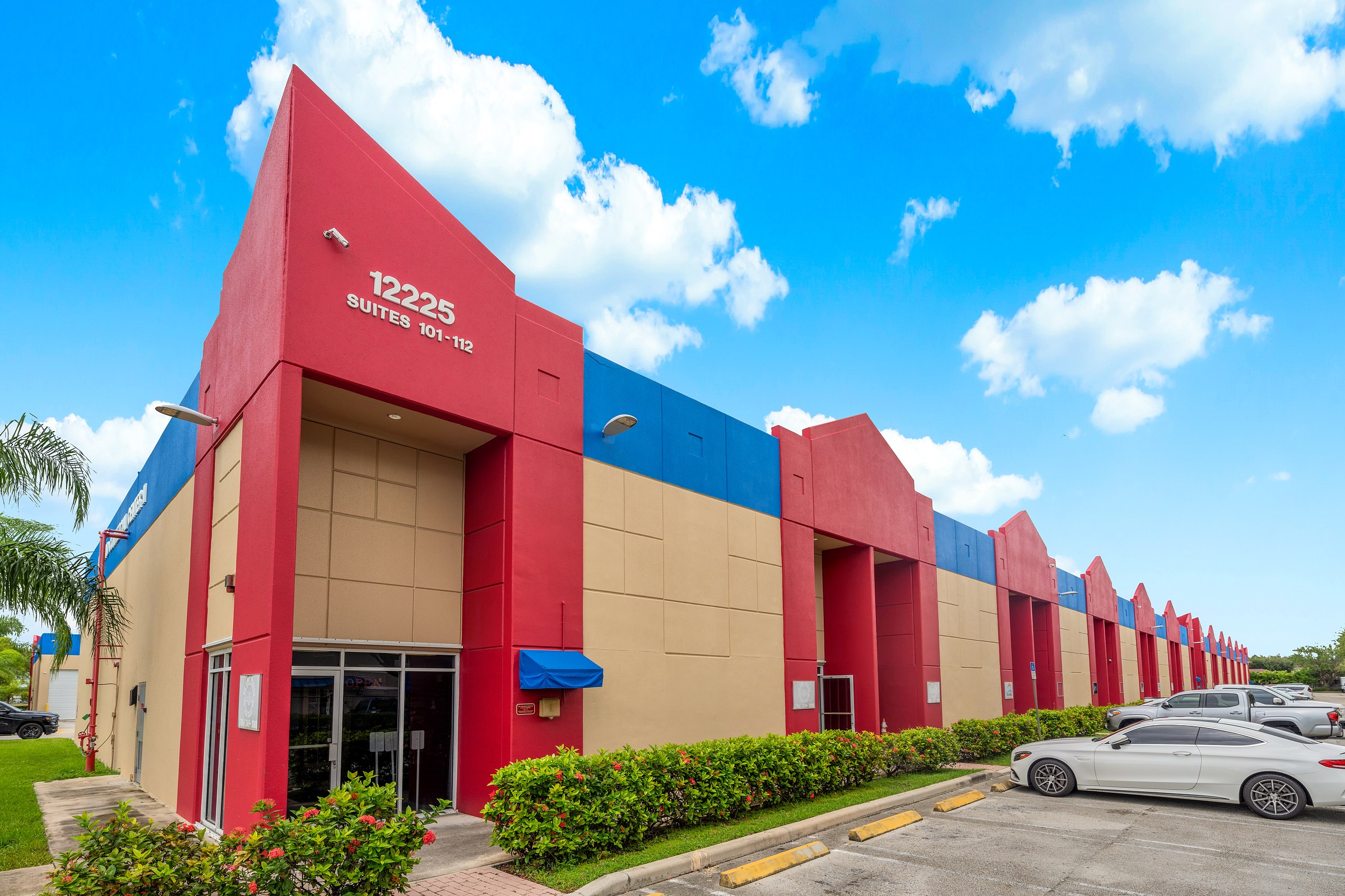 Cortland Commercial Center II at 12225 SW 128th Street: red entry towers, blue parapet bands and sand stucco under a blue sky