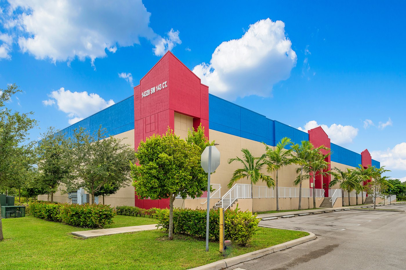 Red entry tower marked 14320 SW 143 Ct., the largest Zacarias IV building, with landscaping and palm trees, Zacarias Commercial Center IV